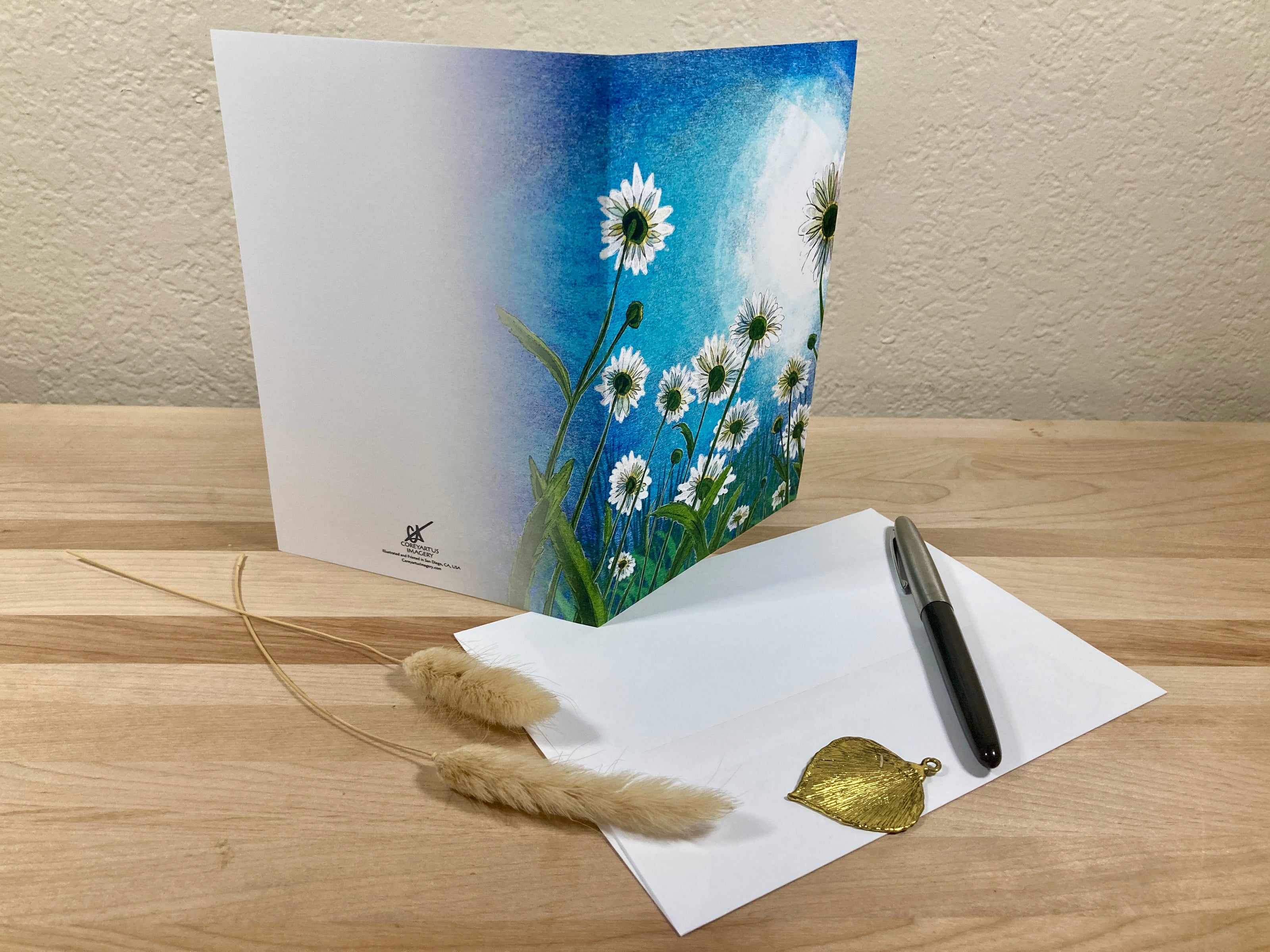 Greeting card with floral design, pen, and decorative leaves on a wooden surface