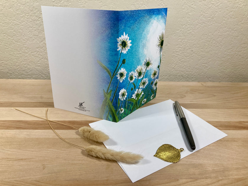 Greeting card with floral design, pen, and decorative leaves on a wooden surface