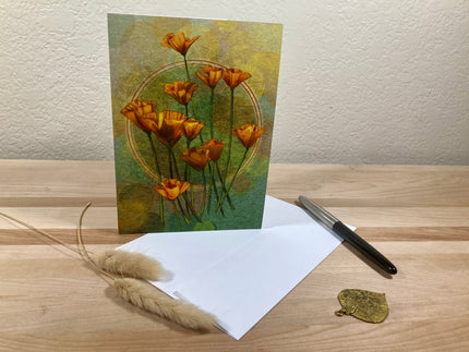 Greeting card with floral design, envelope, pen, and decorative leaf on a wooden surface.
