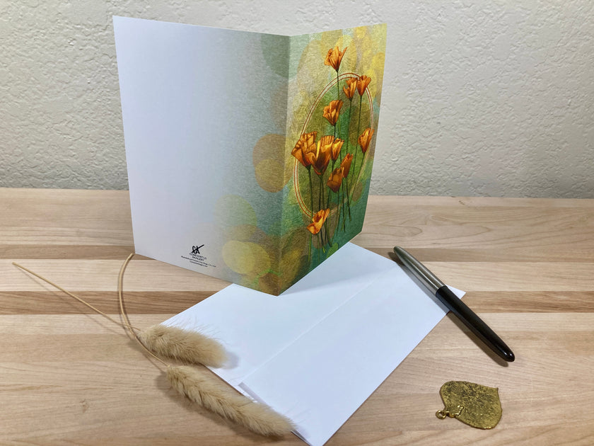 Greeting card with floral design on a wooden surface with a pen and decorative leaf.