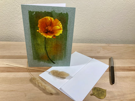 Greeting card with a yellow flower on a wooden surface with an envelope and pen.