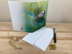 Greeting card with a bird design on a wooden surface with a pen and decorative items.