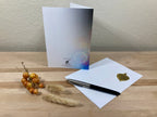 Greeting card, pen, and decorative items on a wooden surface with a neutral background