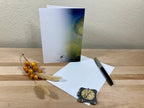Greeting card, pen, and decorative clock on a wooden surface with a neutral background