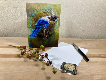 Greeting card with a bird design, pen, envelope, and decorative items on a wooden surface.