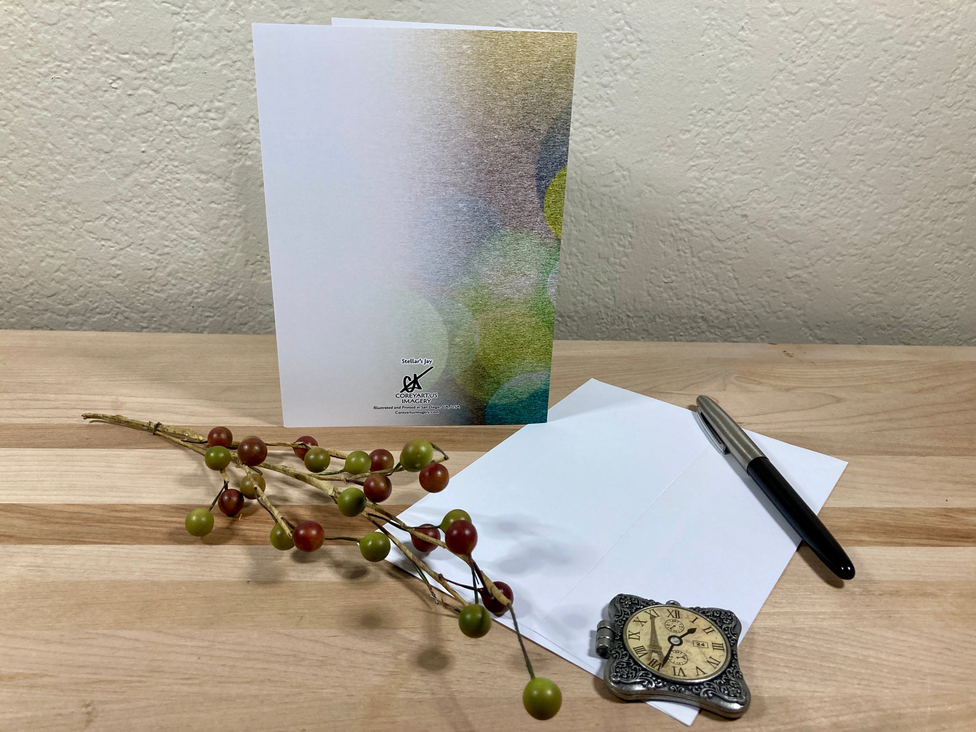 Back of a greeting card displayed with a pen, decorative clock, and small branches on a wooden surface with a neutral background