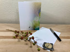 Back of a greeting card displayed with a pen, decorative clock, and small branches on a wooden surface with a neutral background