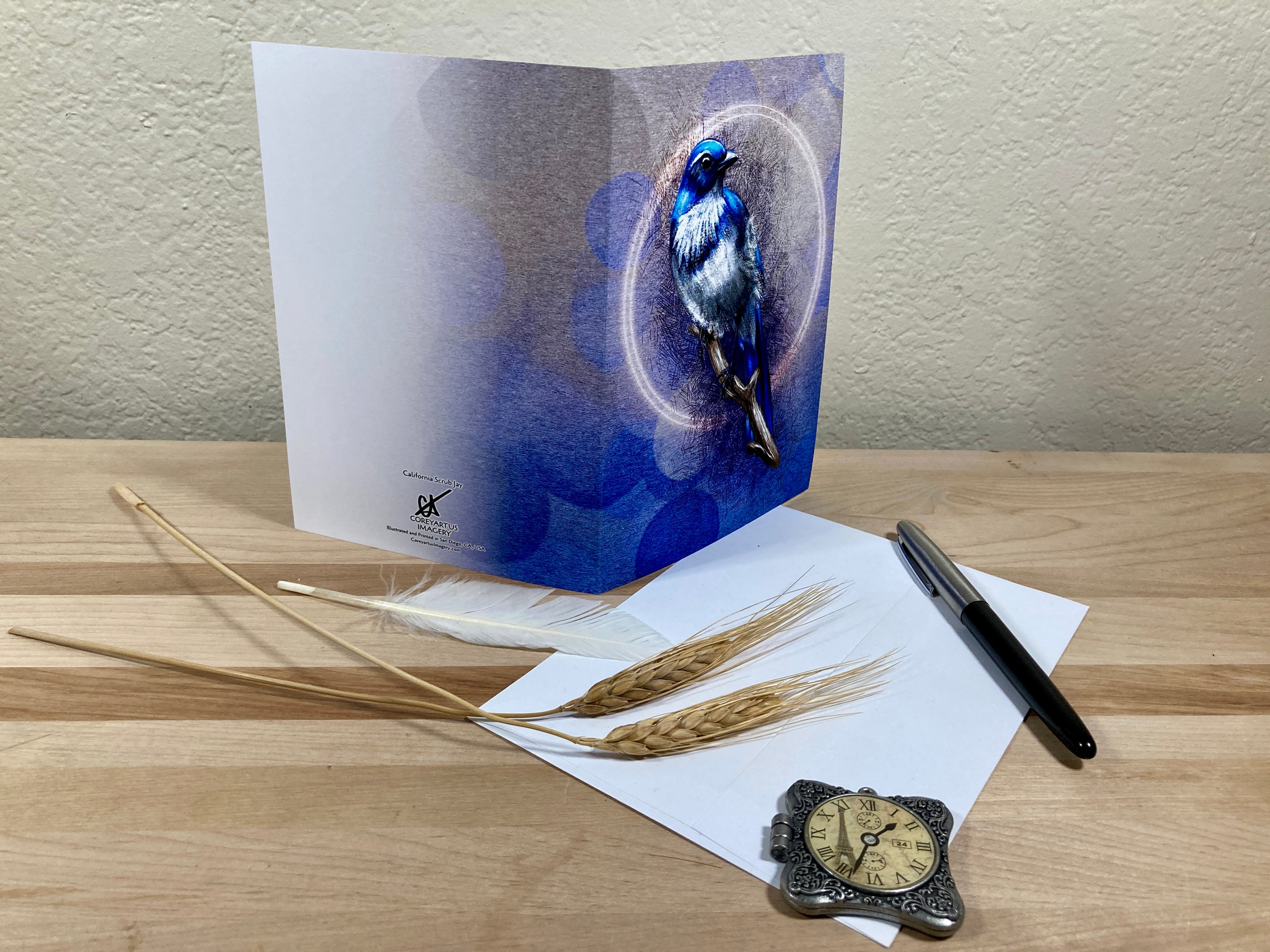 Greeting card with a blue bird design on a wooden surface with a pen and decorative items.