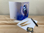 Greeting card with a blue bird design on a wooden surface with a pen and decorative items.