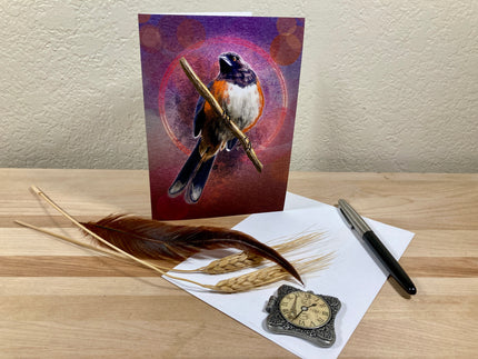 Greeting card with a bird design on a wooden surface with feathers and a pen.