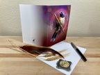 Greeting card with a bird design on a wooden surface with feathers and a pen.