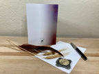 Backside of a greeting card displayed with a pen, feather, and decorative item on a wooden surface with a neutral background