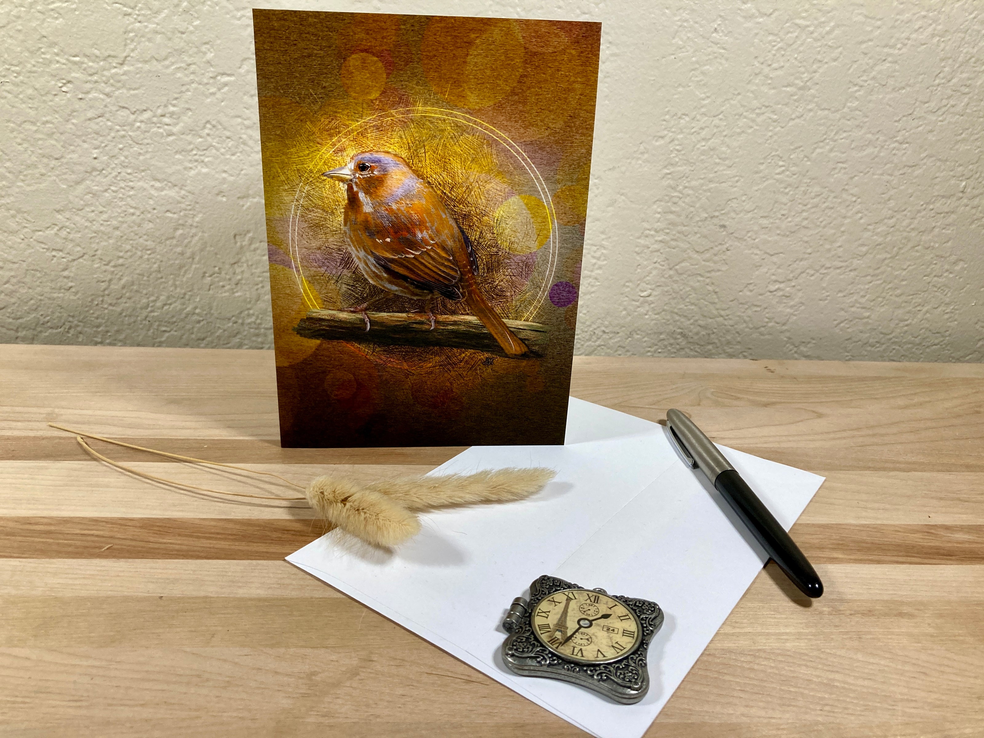 Greeting card with a bird design on a wooden surface with a pen and decorative items.
