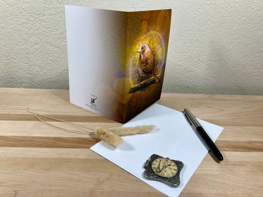 Greeting card with a bird design on a wooden surface with a pen and feather.