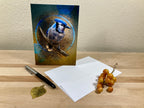 Greeting card with a blue jay design on a wooden surface with a pen and grapes.