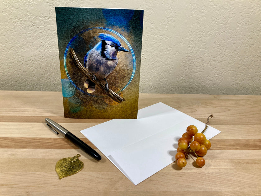 Greeting card with a blue jay design on a wooden surface with a pen and grapes.
