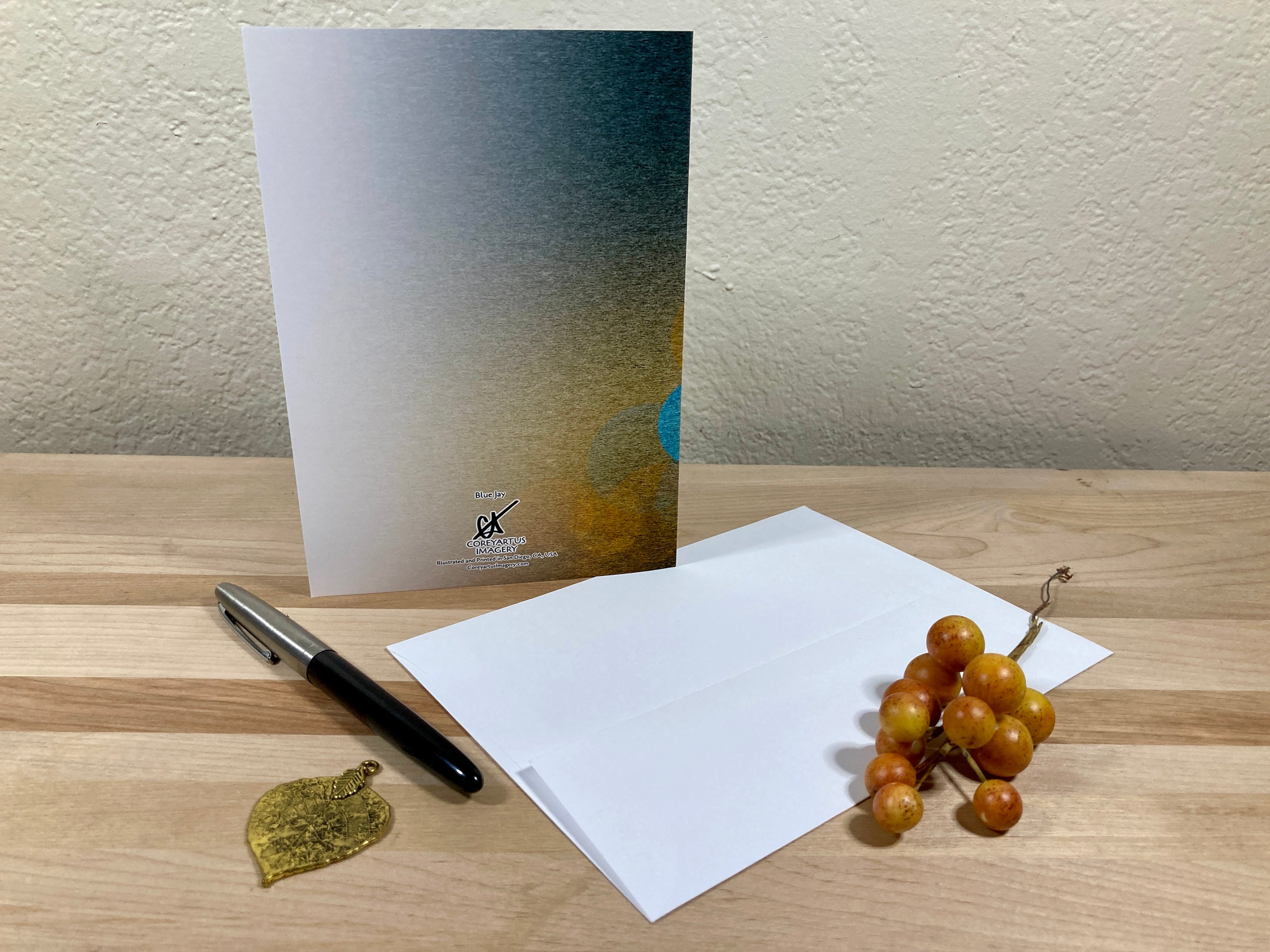 Greeting card, pen, and decorative items on a wooden surface with a neutral background