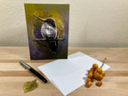 Greeting card with a bird design on a wooden surface with a pen and small plant.