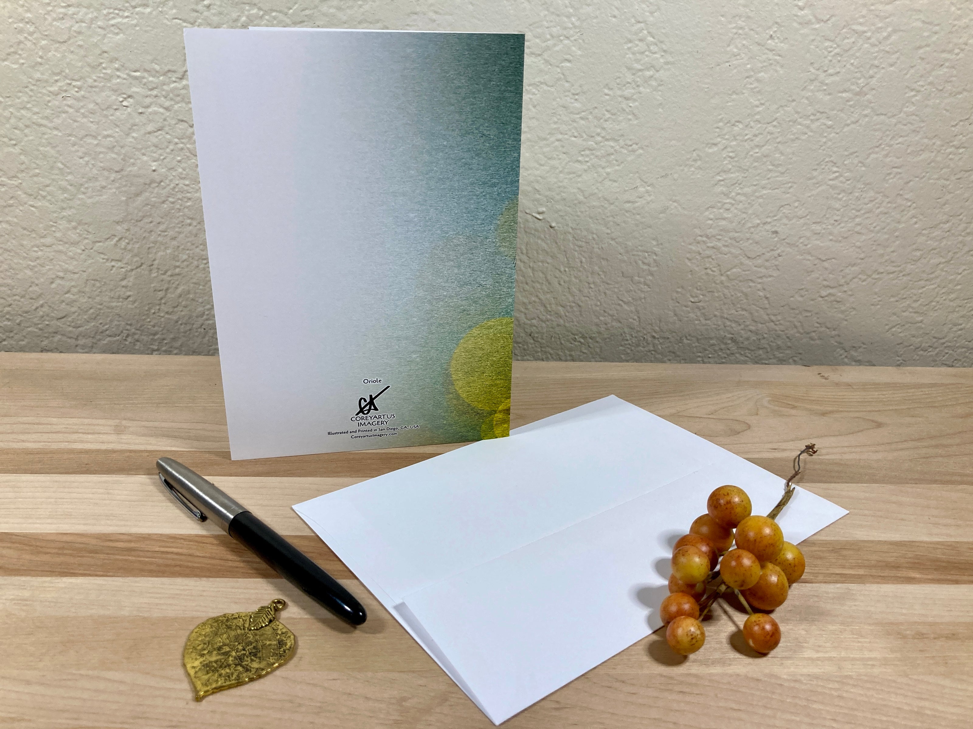 Greeting card, pen, and small plant on a wooden surface with a neutral background