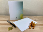 Greeting card, pen, and small plant on a wooden surface with a neutral background
