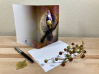 Greeting card with a bird design on a wooden surface with a pen and decorative branch.