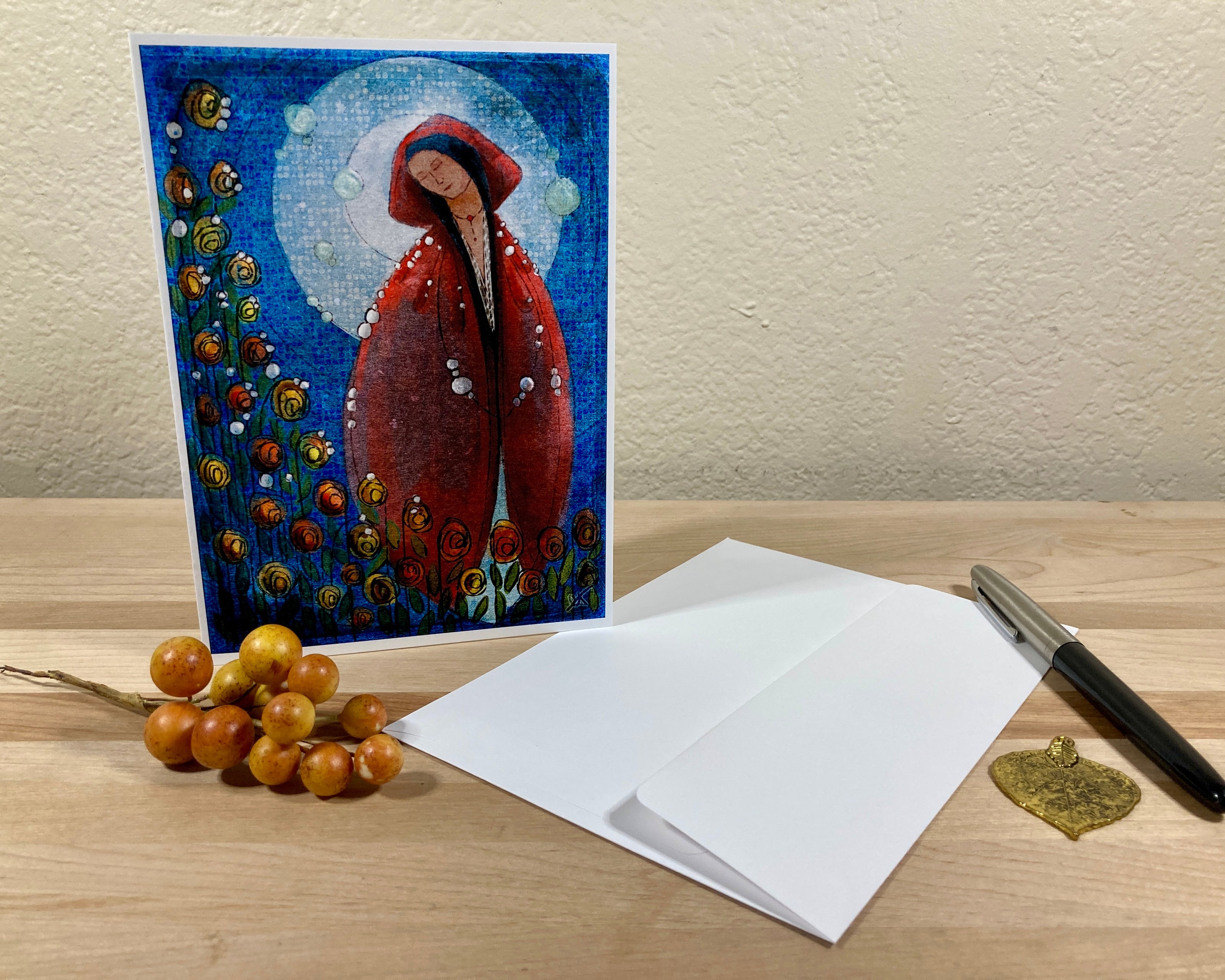Greeting card with a red hooded figure design on a wooden surface with an envelope and pen.