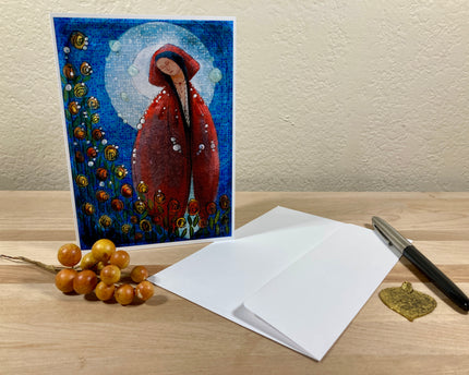 Greeting card with a red hooded figure design on a wooden surface with an envelope and pen.