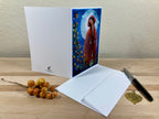 Greeting card with a red-robed figure design on a wooden surface with a pen and berries.