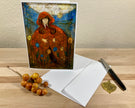 Greeting card with artistic design of a person in a red hood, envelope, pen, and berries on a wooden surface.
