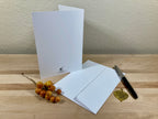 Two white greeting cards on a wooden surface with a pen and decorative elements.