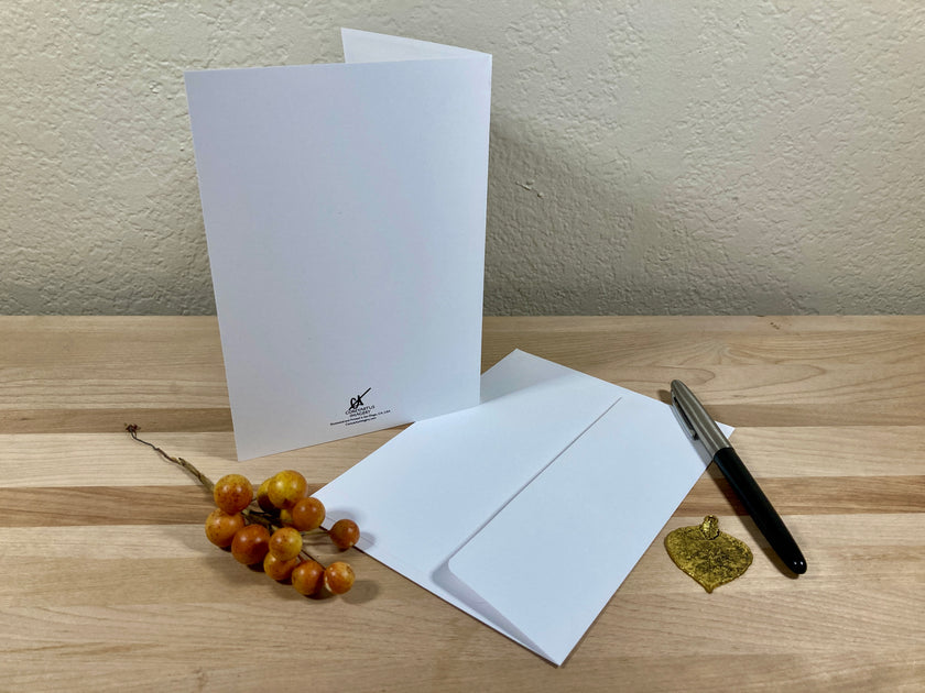 Two white greeting cards on a wooden surface with a pen and decorative elements.