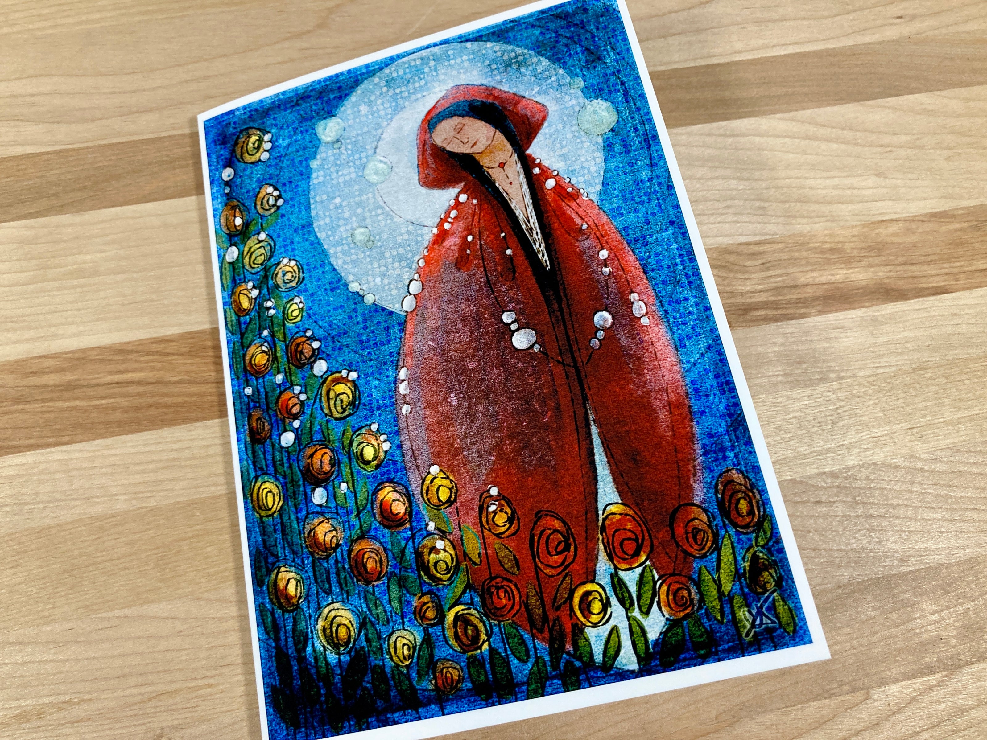 Greeting card with a stylized figure in a red coat and hat, surrounded by flowers on a wooden surface.