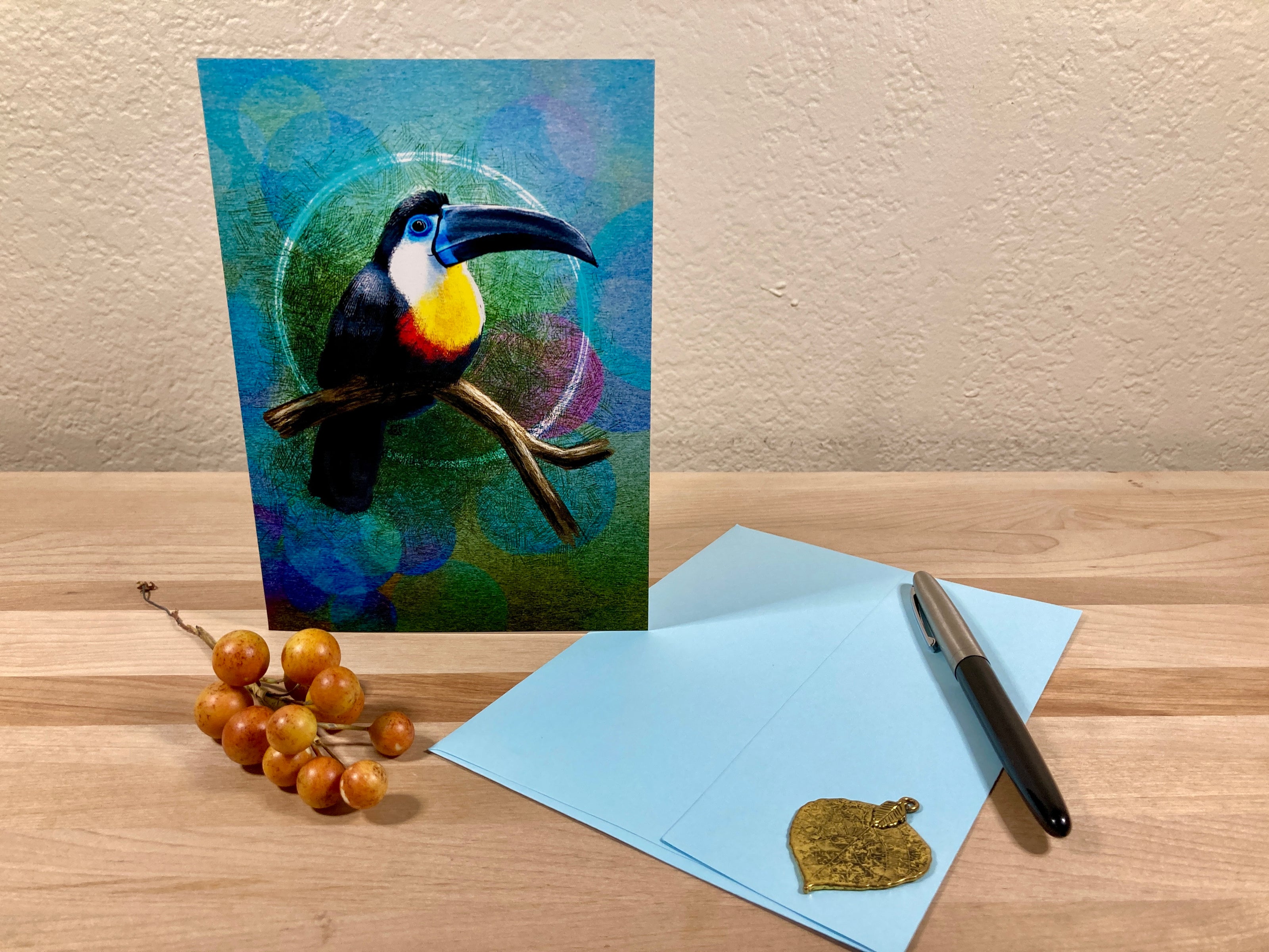 Card with a toucan design on a wooden surface with a pen and small object.