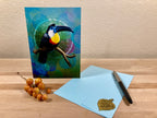 Card with a toucan design on a wooden surface with a pen and small object.
