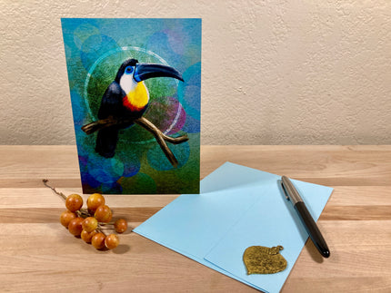 Card with a toucan design on a wooden surface with a pen and small object.