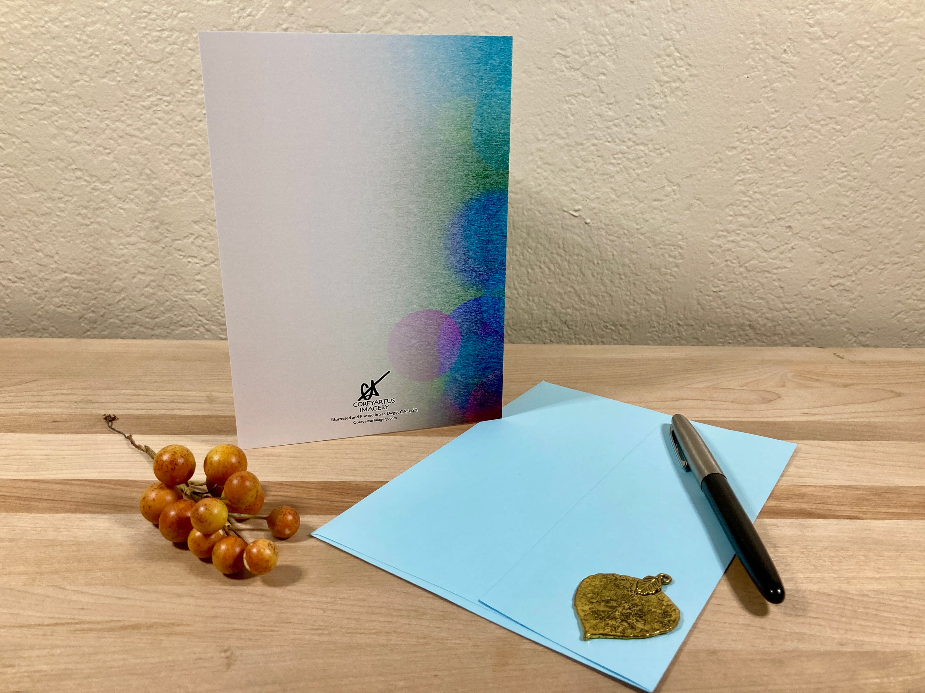 Back of a greeting card displayed with a pen, and small object on a wooden surface with a textured wall background