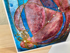 Decorative tile with abstract design featuring gold lines and a pinkish-red center on a blue background.
