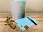 The back of a greeting card displayed on a wooden surface with a pen and decorative elements.