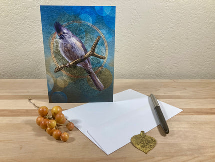 Greeting card with a bird design on a wooden surface with stationery items.