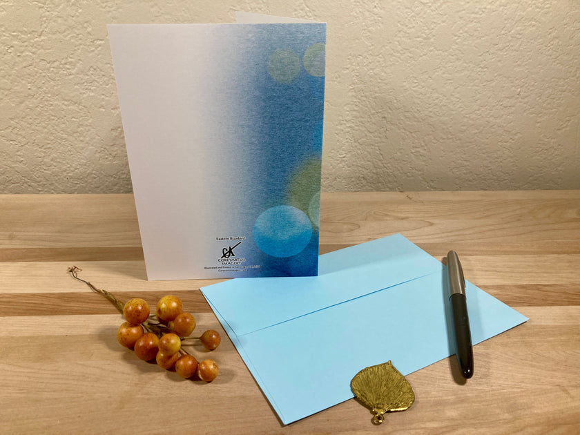Greeting card with blue design, envelope, pen, and decorative elements on a wooden surface.