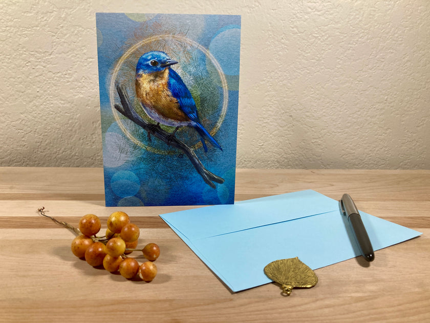 Greeting card with a blue bird illustration on a wooden surface with an envelope and pen.