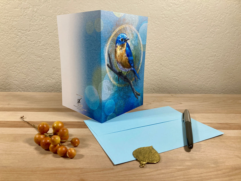Greeting card with a blue bird design on a wooden surface with an envelope and decorative items.