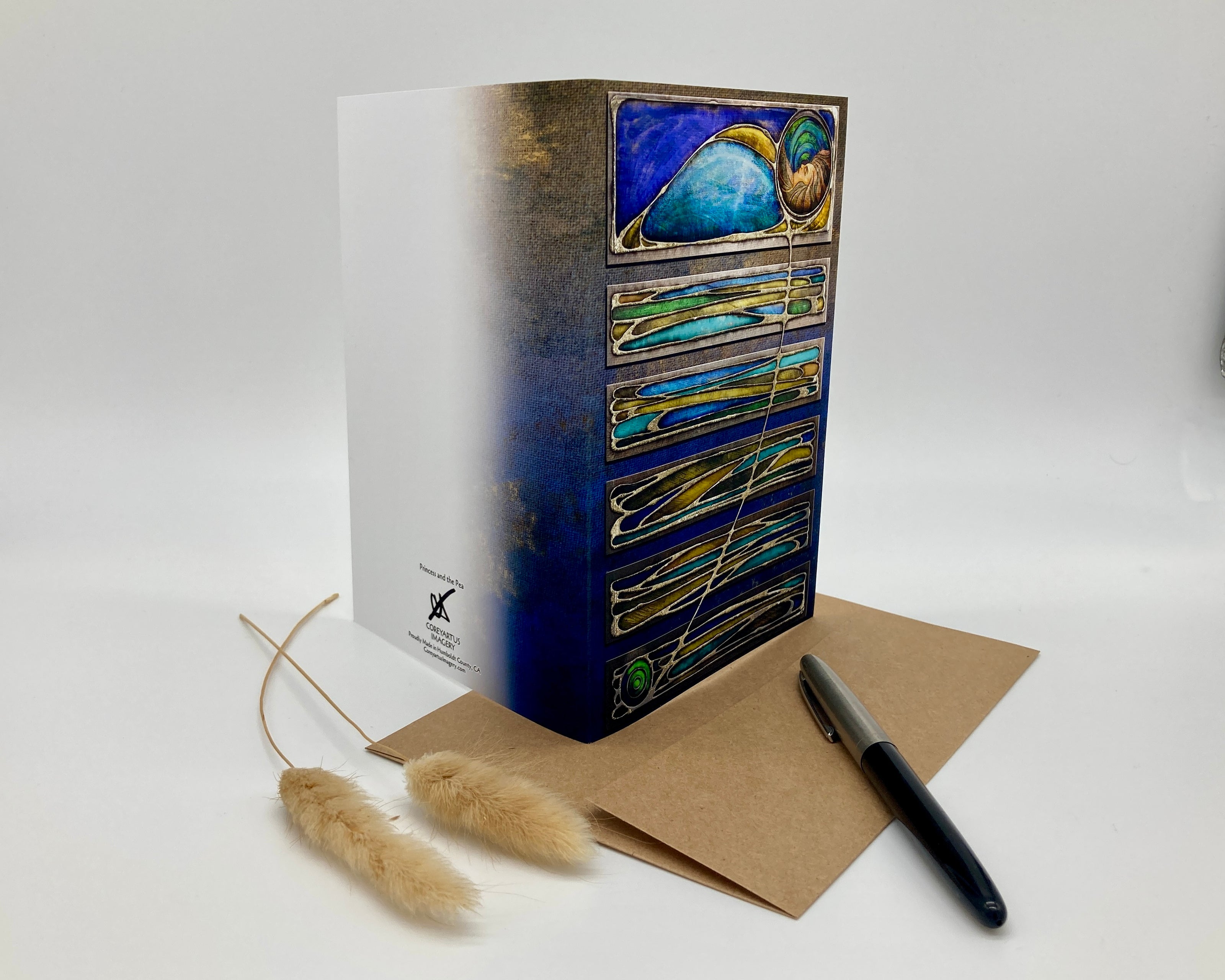 Decorative box with artistic design, a pen, and a card on a white background