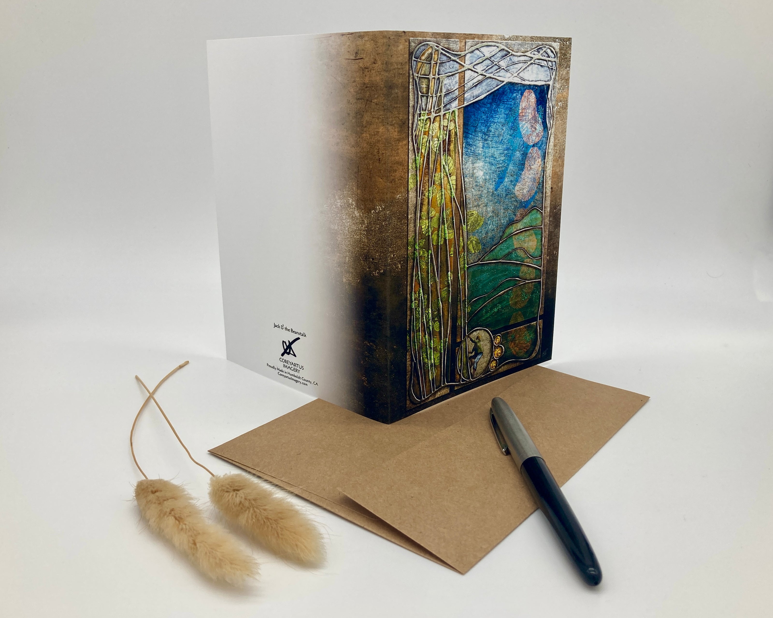 Decorative greeting card with artistic design, pen, and dried plant on a white background