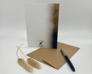 Greeting card, pen, and dried plant on a white background