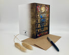 Decorative book with artistic cover design, accompanied by a pen and card on a white background