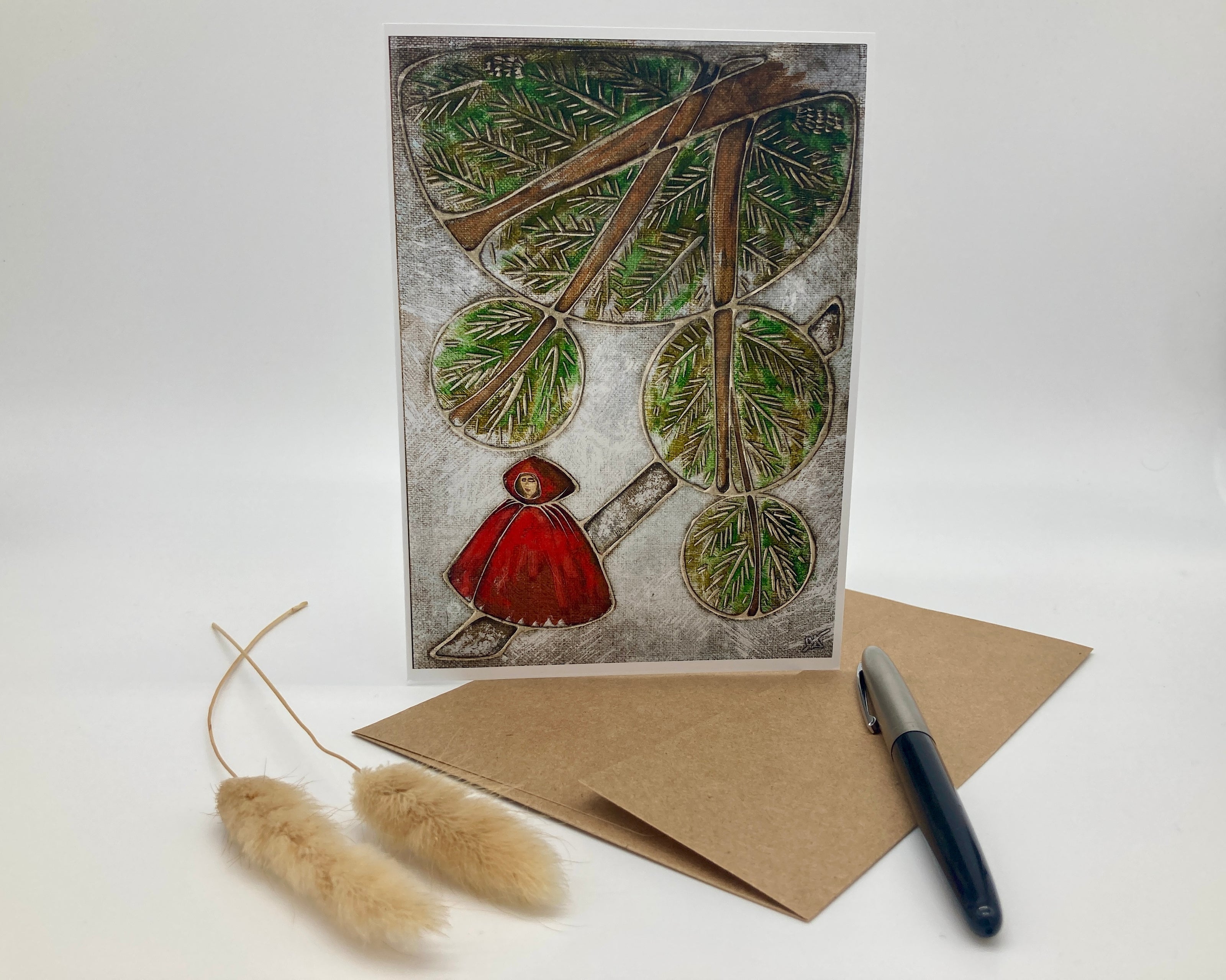 Greeting card with nature-themed design featuring a person in a red coat and branches, accompanied by a pen and envelope on a white background.