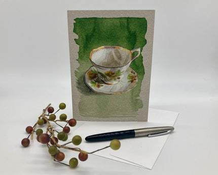 Greeting card with teacup design, pen, and decorative branch on a white background