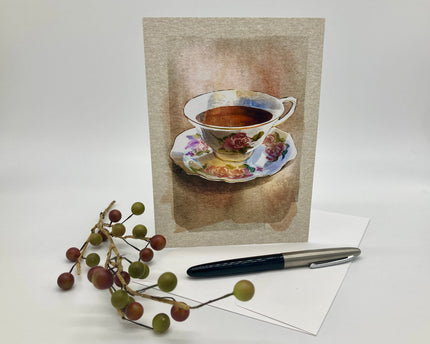 Greeting card with a teacup design on a white surface with a pen and decorative branch.