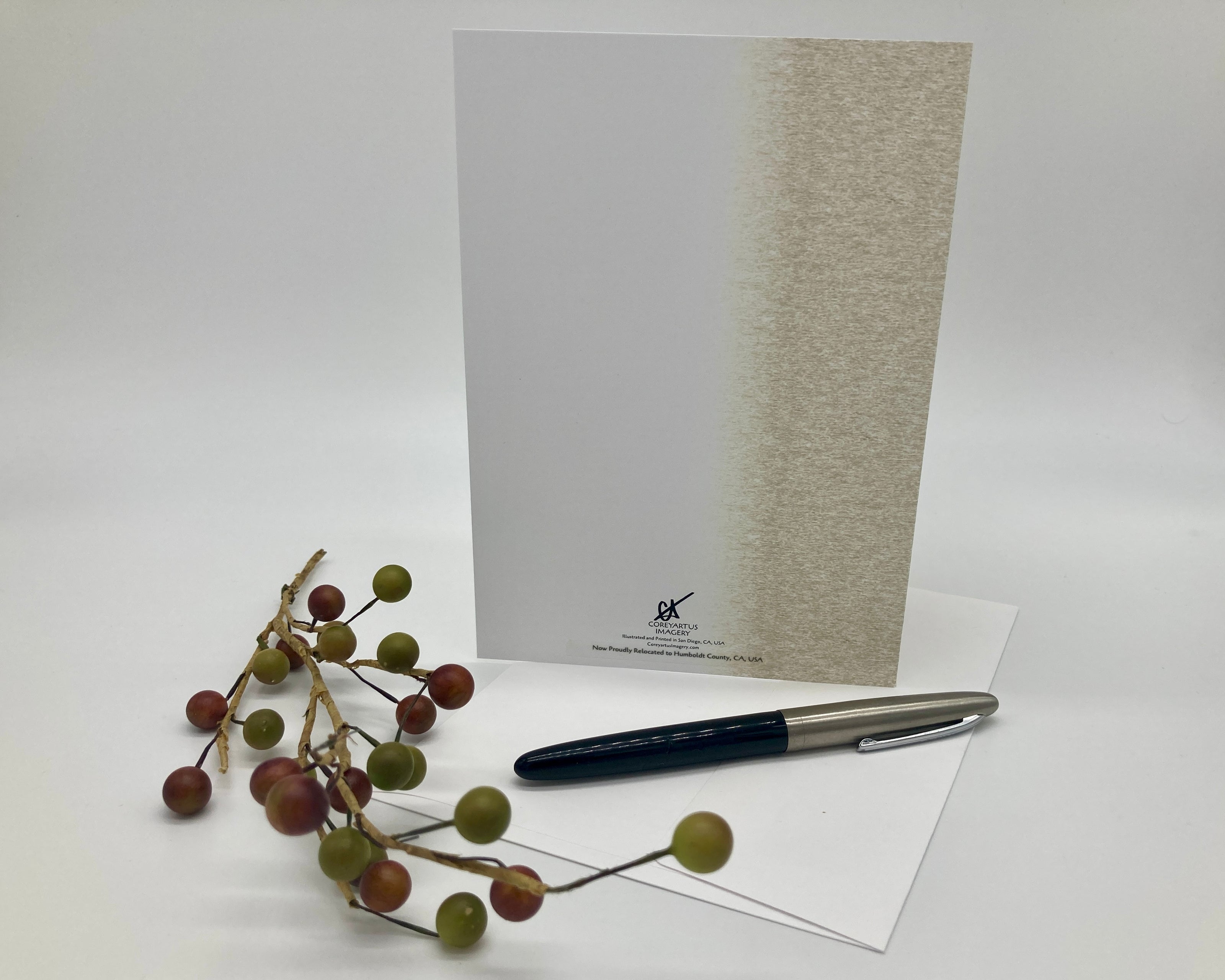 Back of a greeting card displayed with a pen, and decorative branch on a white surface